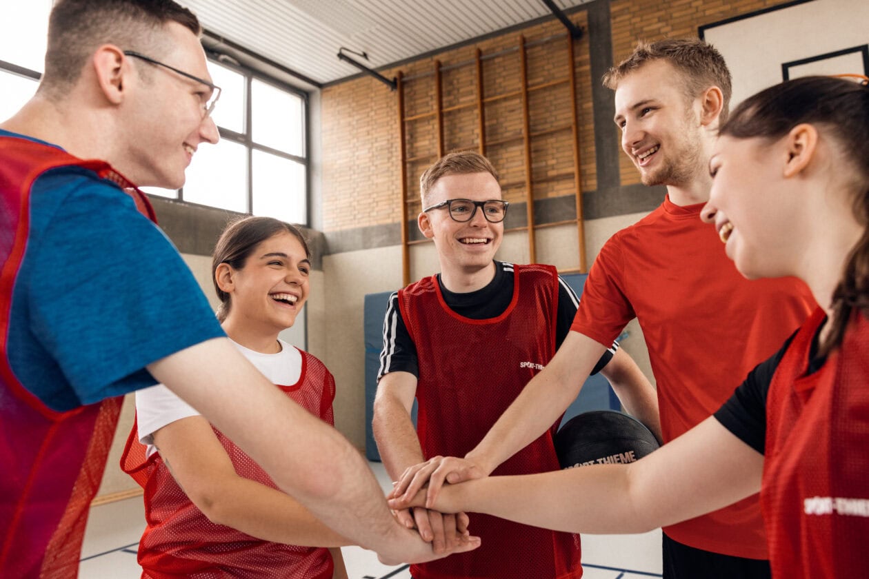 Five trainees from Sport-Thieme are standing together in a circle during trainee sports.