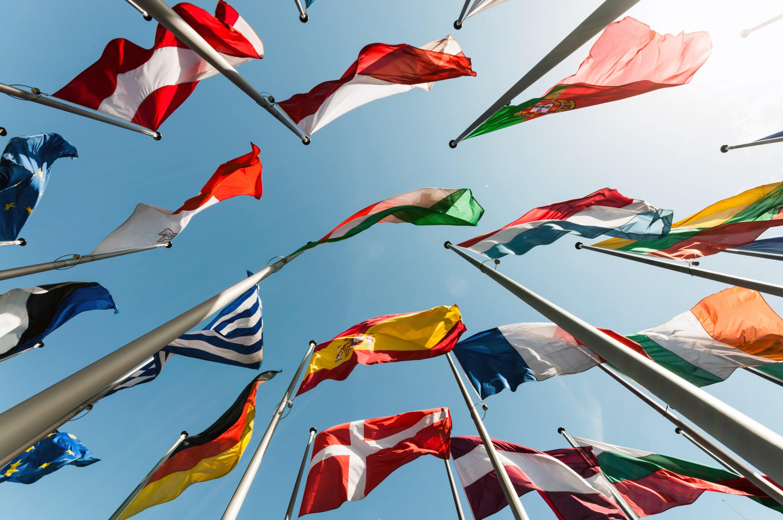Various international flags fluttering on tall flagpoles against a clear blue sky.