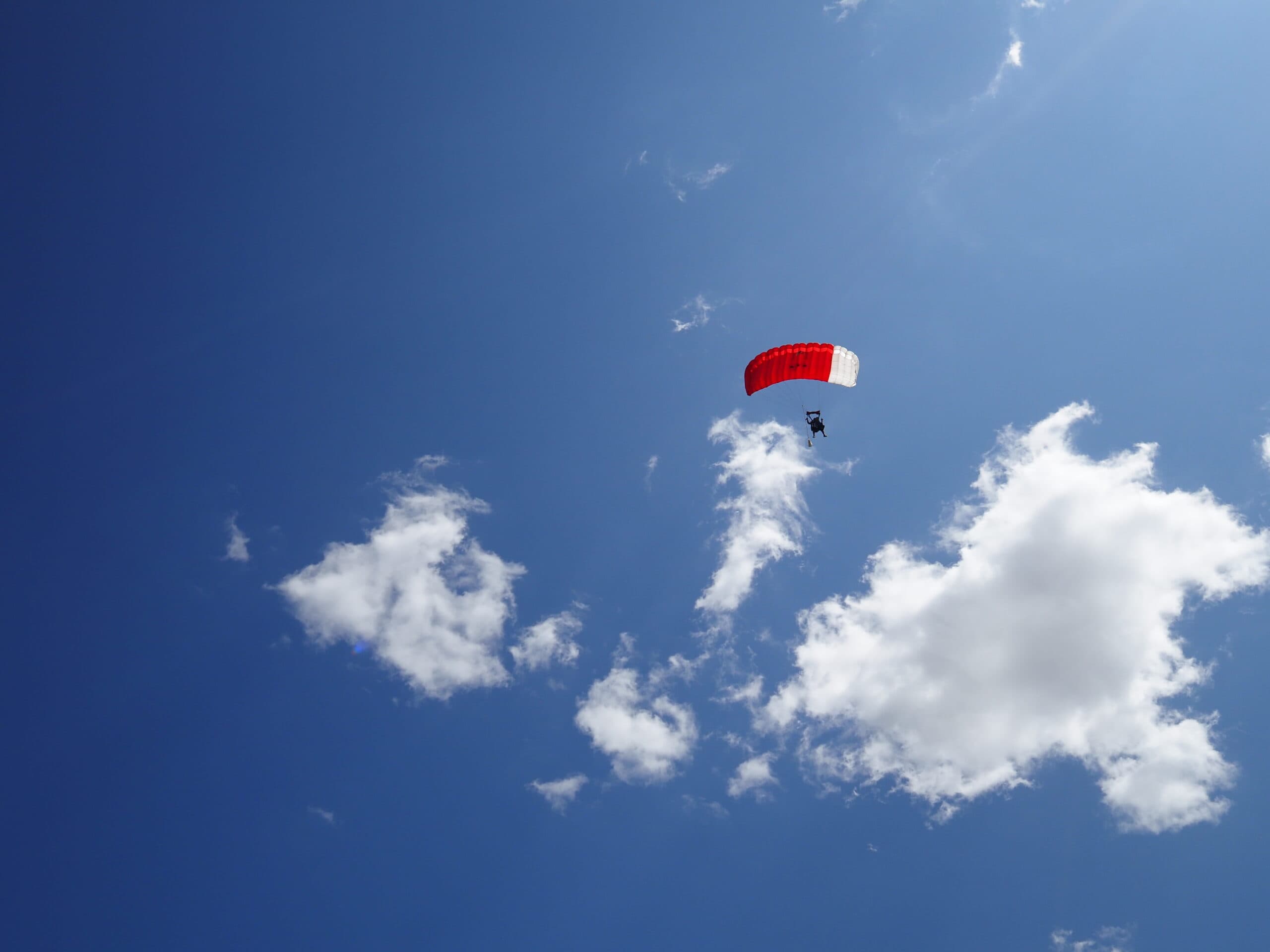 A skydiver floats with a red and white parachute in the clear sky.