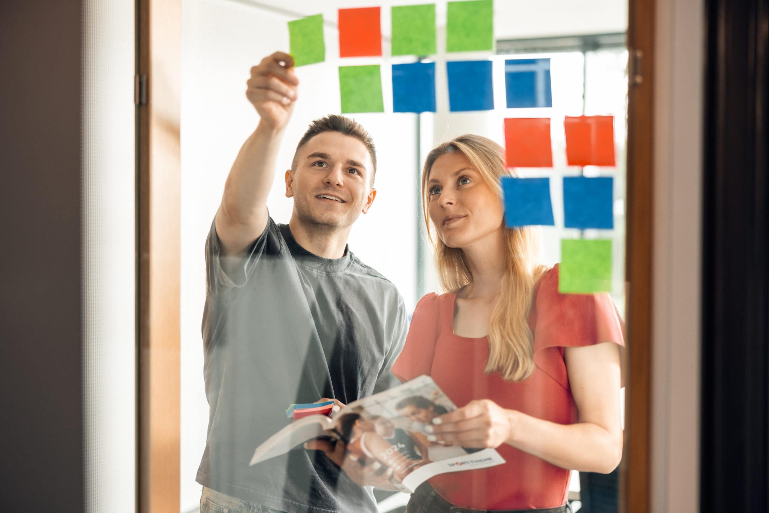 Marketing trainees planning a campaign using Post-its on a glass wall.