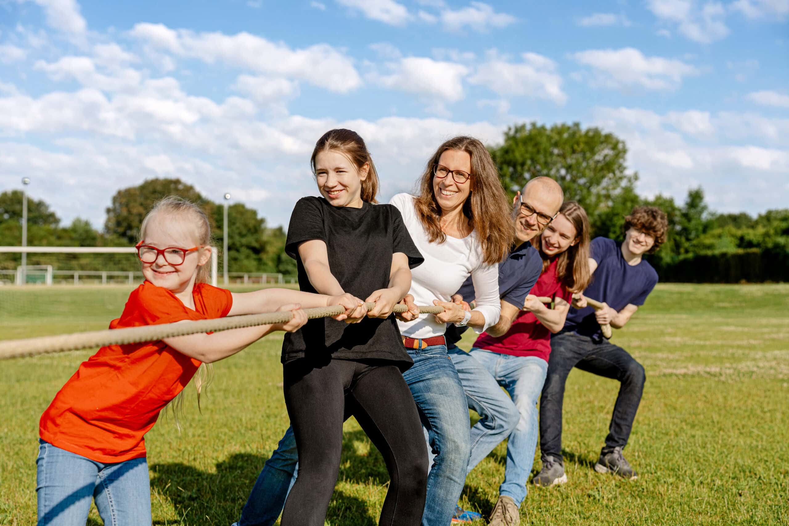 The Sport-Thieme family, management and children pulling a rope together on a grassy field.