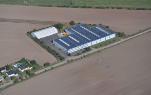 Aerial view of one of the Sport-Thieme warehouse buildings with solar panels on the roof, surrounded by agricultural fields and a storage tent.