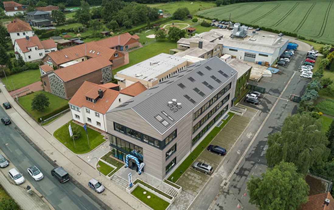 Aerial view of the modern Sport-Thieme company building with an adjacent parking lot and surrounding buildings.