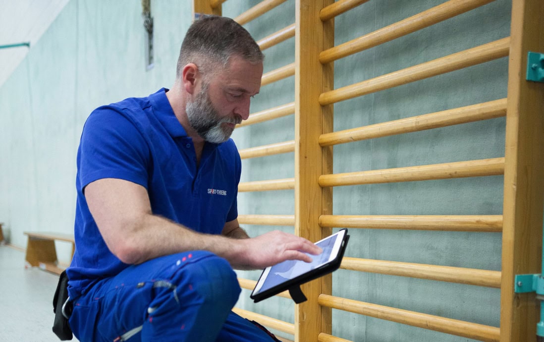 A Sport-Thieme service employee checks a wall bars system in a gym using a tablet.