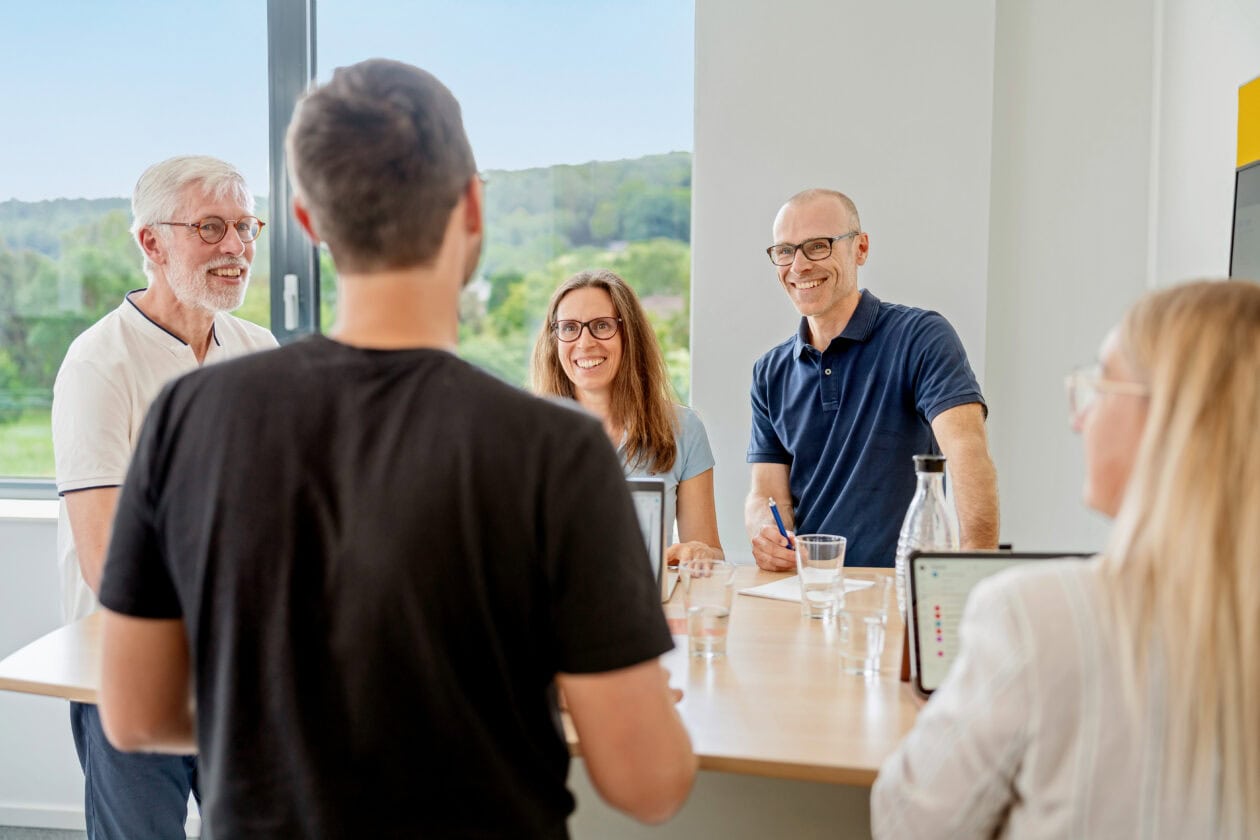 Die Geschäftsleitung von Sport-Thieme steht mit mehreren Mitarbeitenden an einem Tisch.
