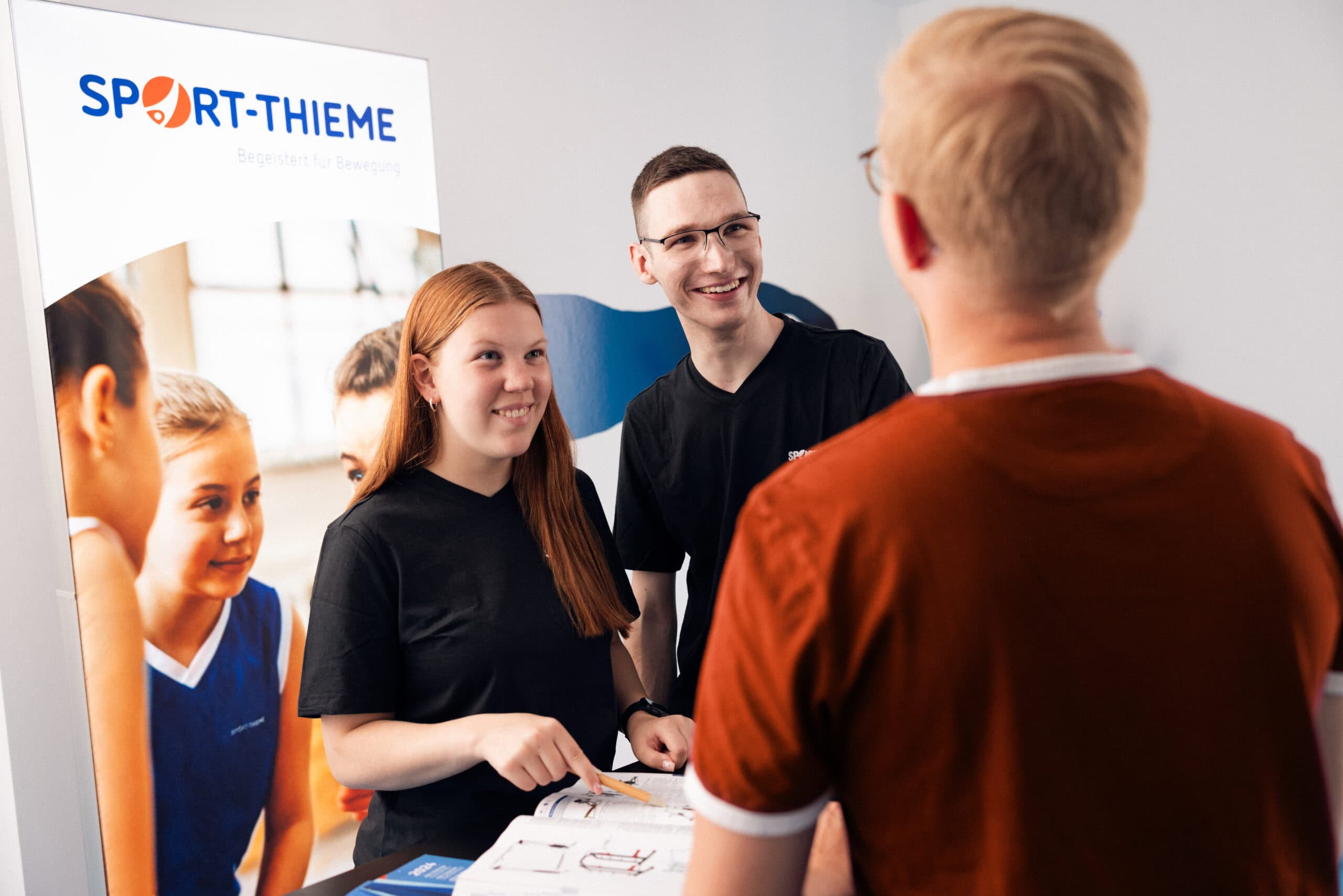 Sport-Thieme employees talking with visitors at a modern trade fair booth during a professional exhibition