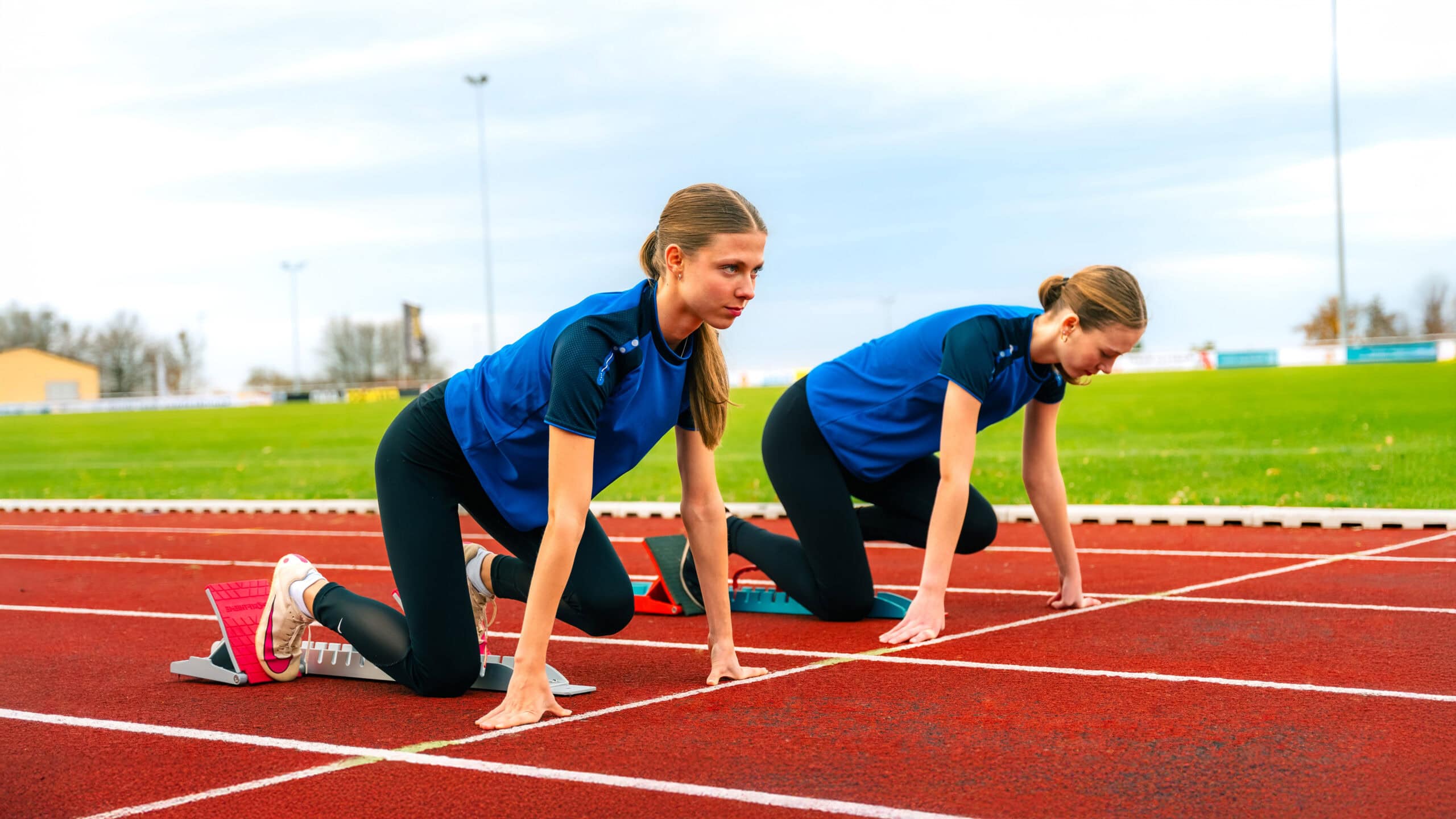Two female runners are in starting position on the track.