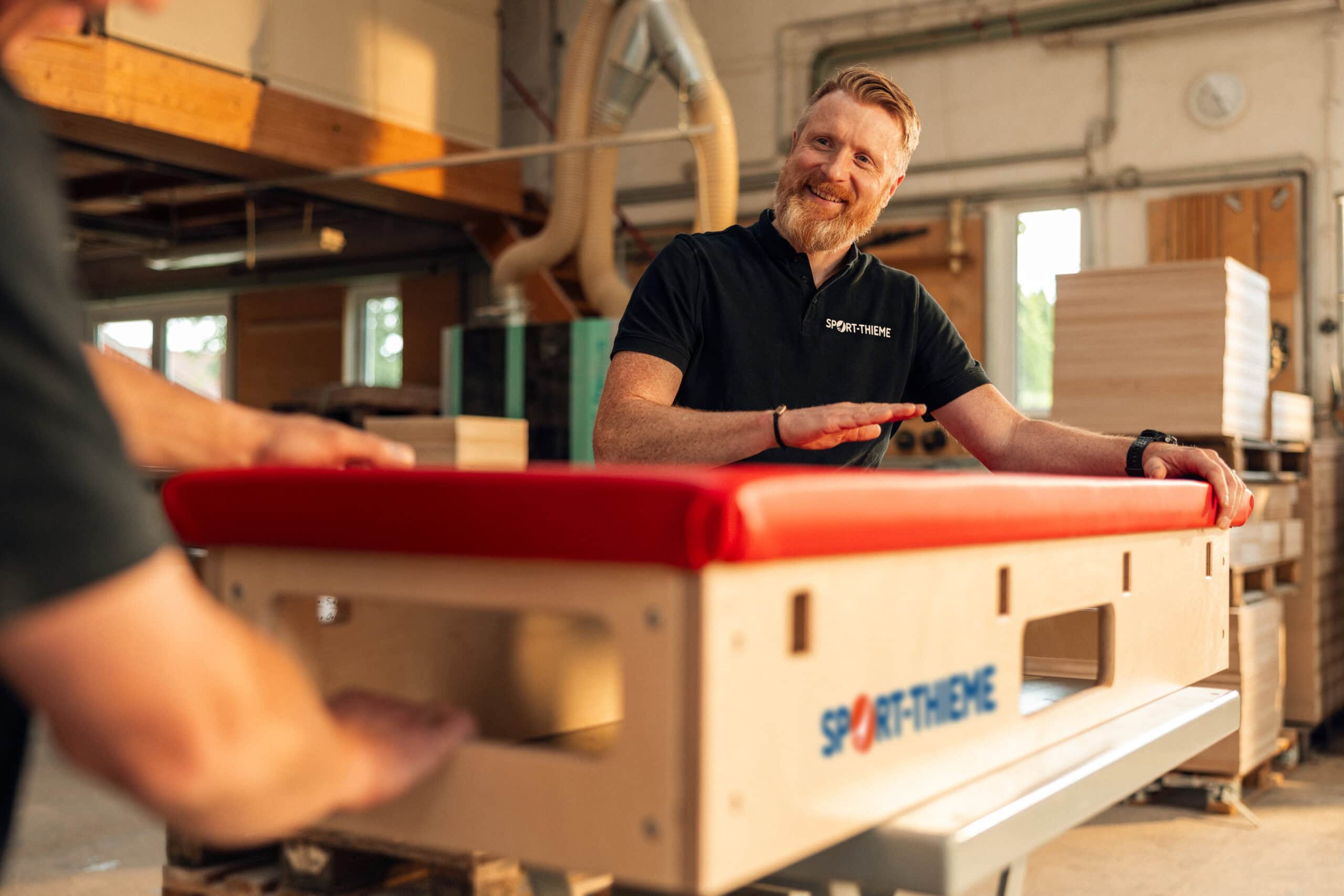 A Sport-Thieme employee in the workshop inspects a newly manufactured vaulting box with red padding.