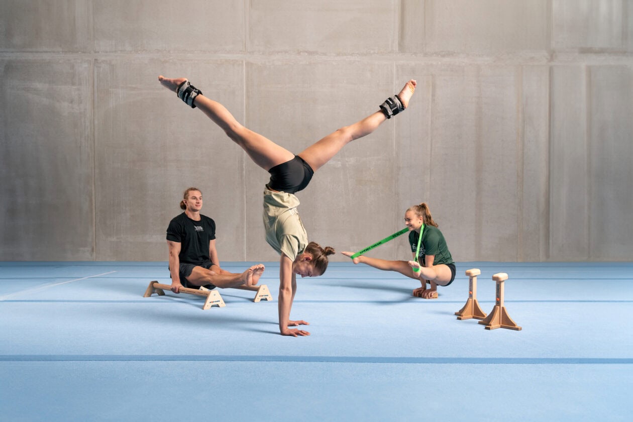 Gymnasts from "Feuerwerk der Turnkunst" training with Sport-Thieme equipment on a blue floor mat.
