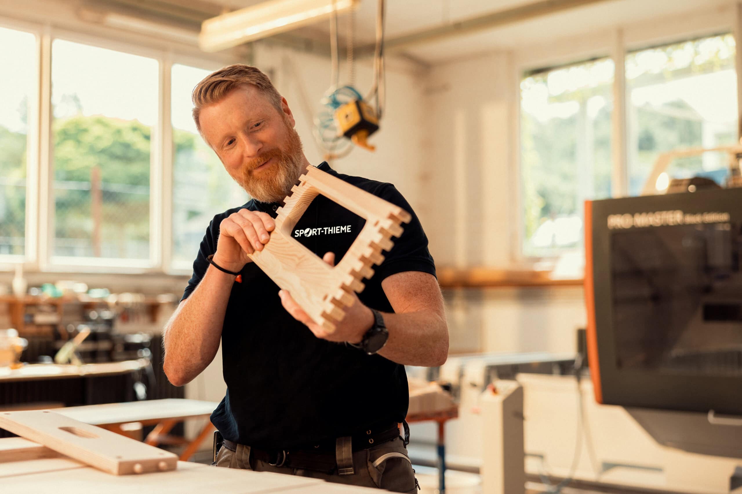 A Sport-Thieme employee inspects a precisely crafted wooden component of a vaulting box in a modern workshop.