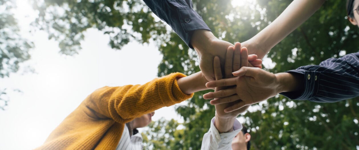 Mehrere Hände von Menschen, die übereinandergelegt sind, als Zeichen von Teamwork.