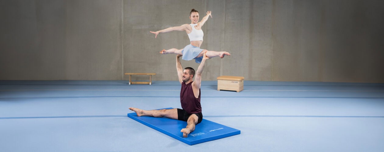 Zwei Sportler, die auf einer Matte Gymnastikübungen machen.