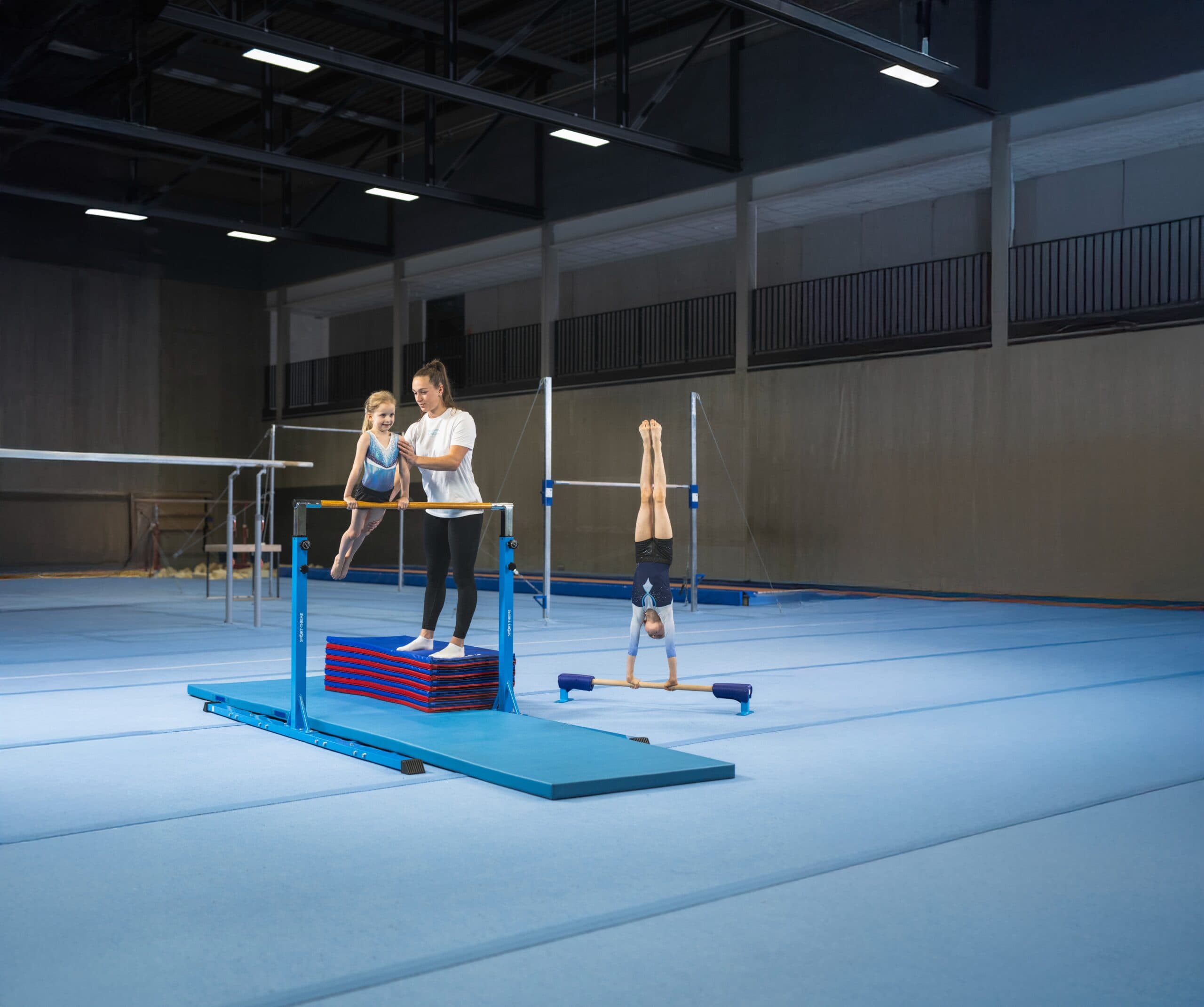 Two children are training on the parallel bars, supported by a coach
