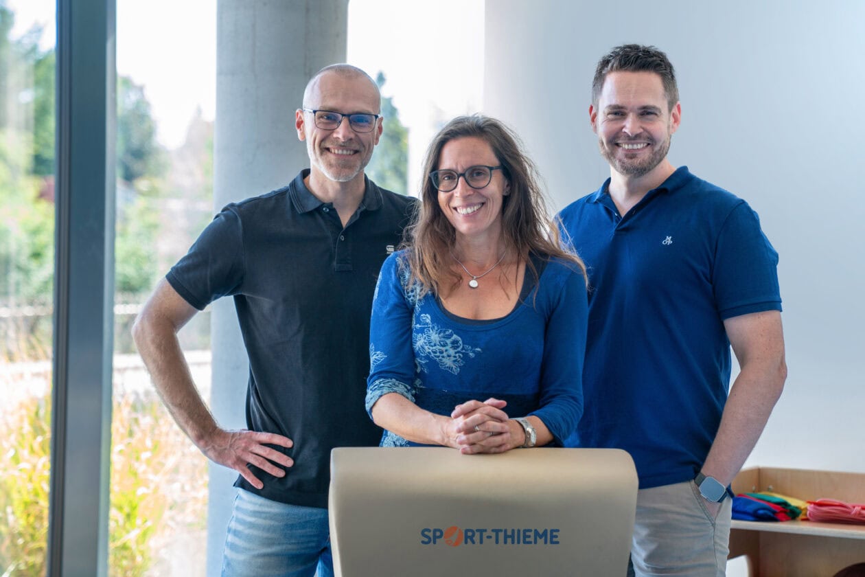 The management team of Sport-Thieme with Maximilian Hohe, Katharina Hohe-Thieme and Michael Egerer stands together in front of a Sport-Thieme bench, looking confidently at the camera.